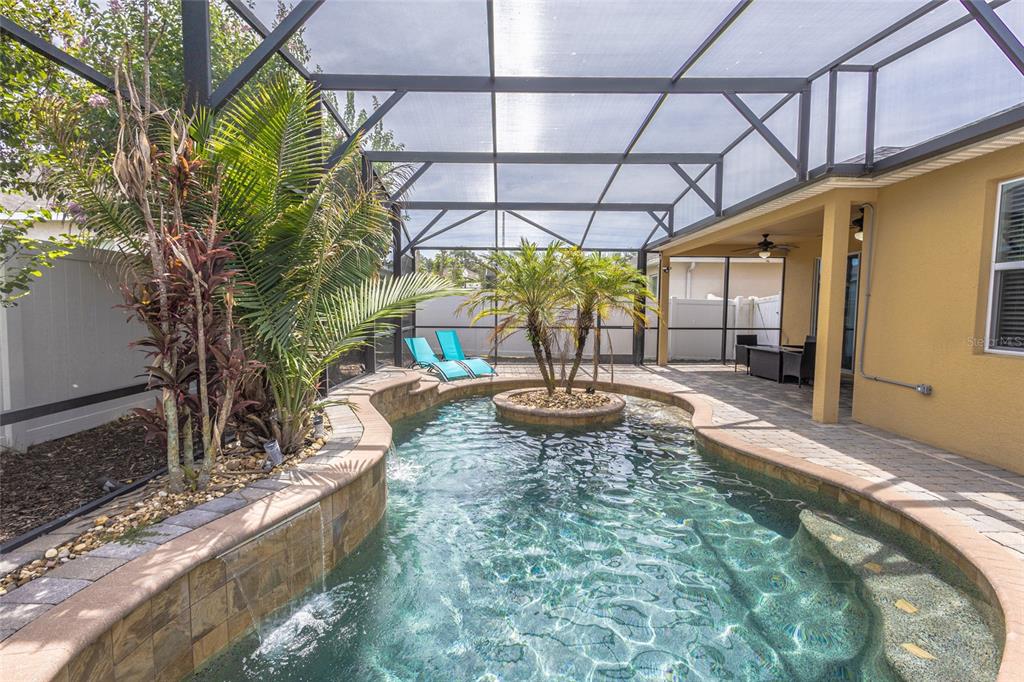 A screened-in patio features a curved swimming pool with a central island and waterfall — 4925 TORTOISE TRAIL, ST CLOUD, FL