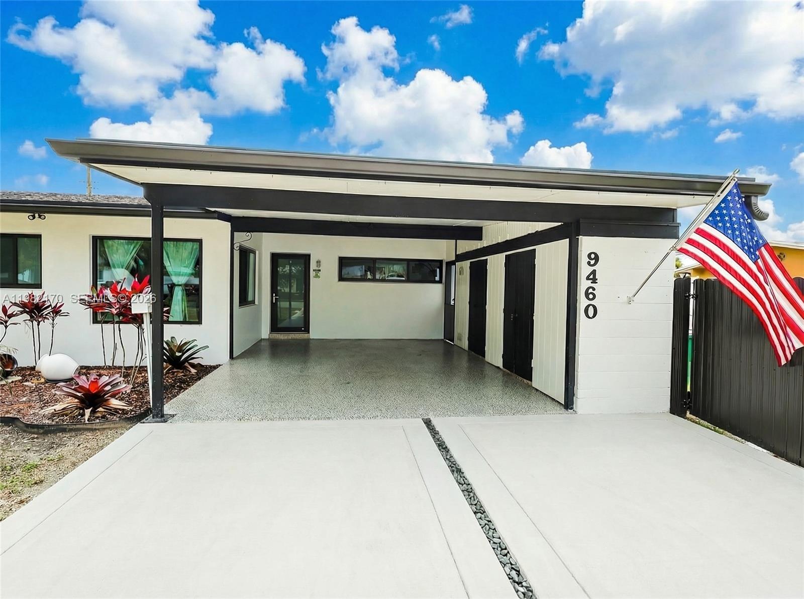 A white house exterior features a covered carport, a concrete driveway, and an American flag — 9460 Martinique Dr, Cutler Bay FL 33189, CUTLER BAY, FL