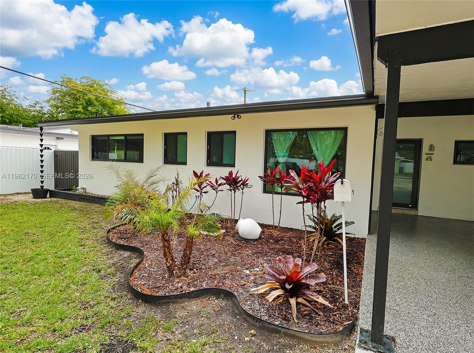 A white house exterior features a landscaped garden bed with tropical plants and a mailbox — 9460 Martinique Dr, Cutler Bay FL 33189, CUTLER BAY, FL