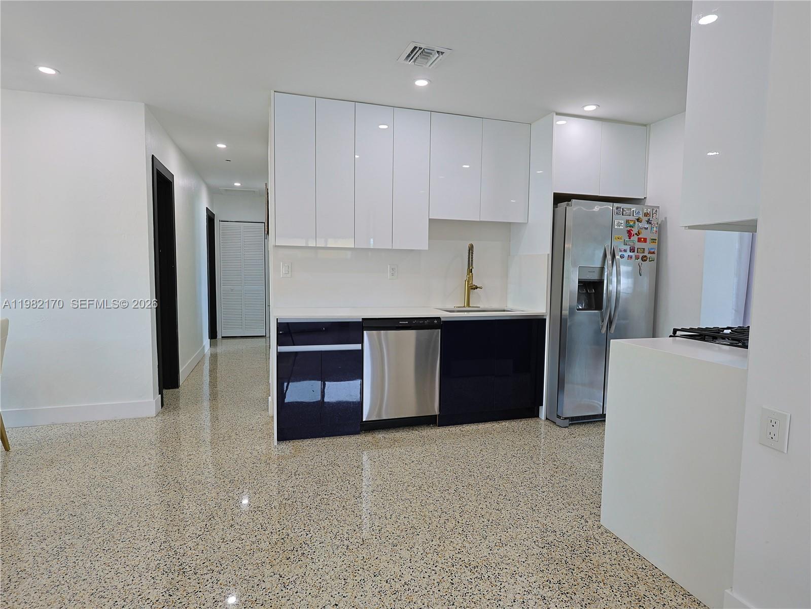 A kitchen features white upper cabinets, dark lower cabinets, stainless steel appliances, and terrazzo flooring — 9460 Martinique Dr, Cutler Bay FL 33189, CUTLER BAY, FL