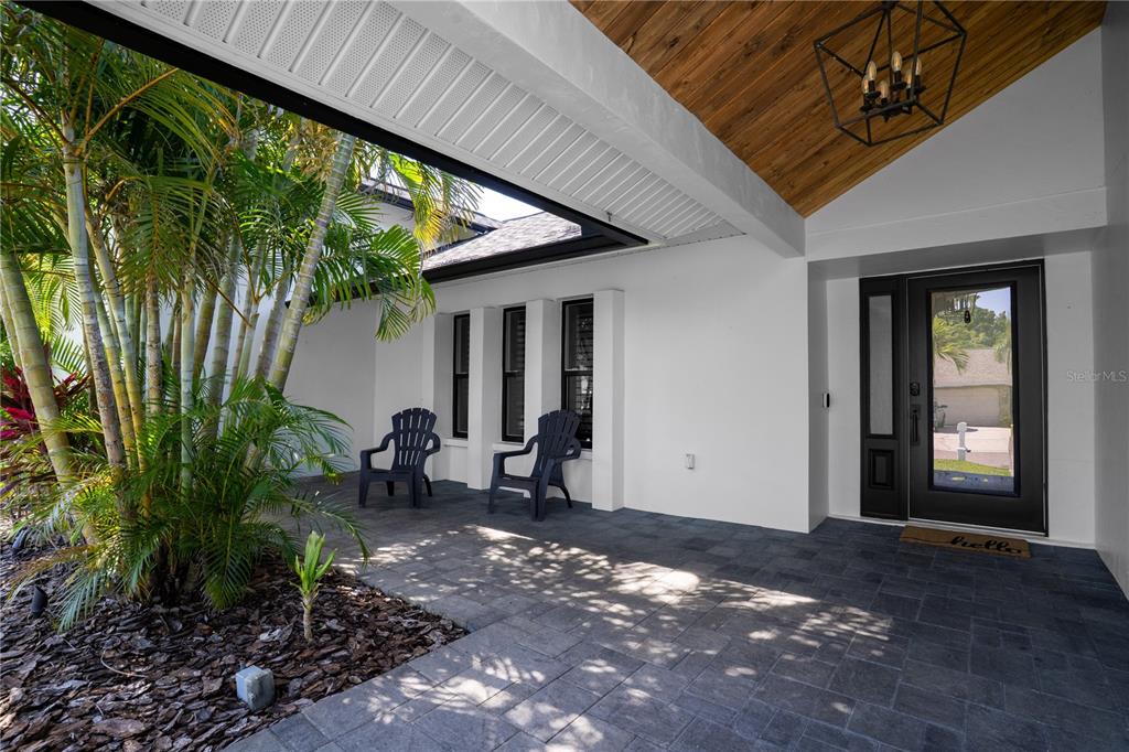 A covered patio features dark pavers, two chairs, and a wood-paneled ceiling near the entrance — 11763 HARBORSIDE CIRCLE, LARGO, FL