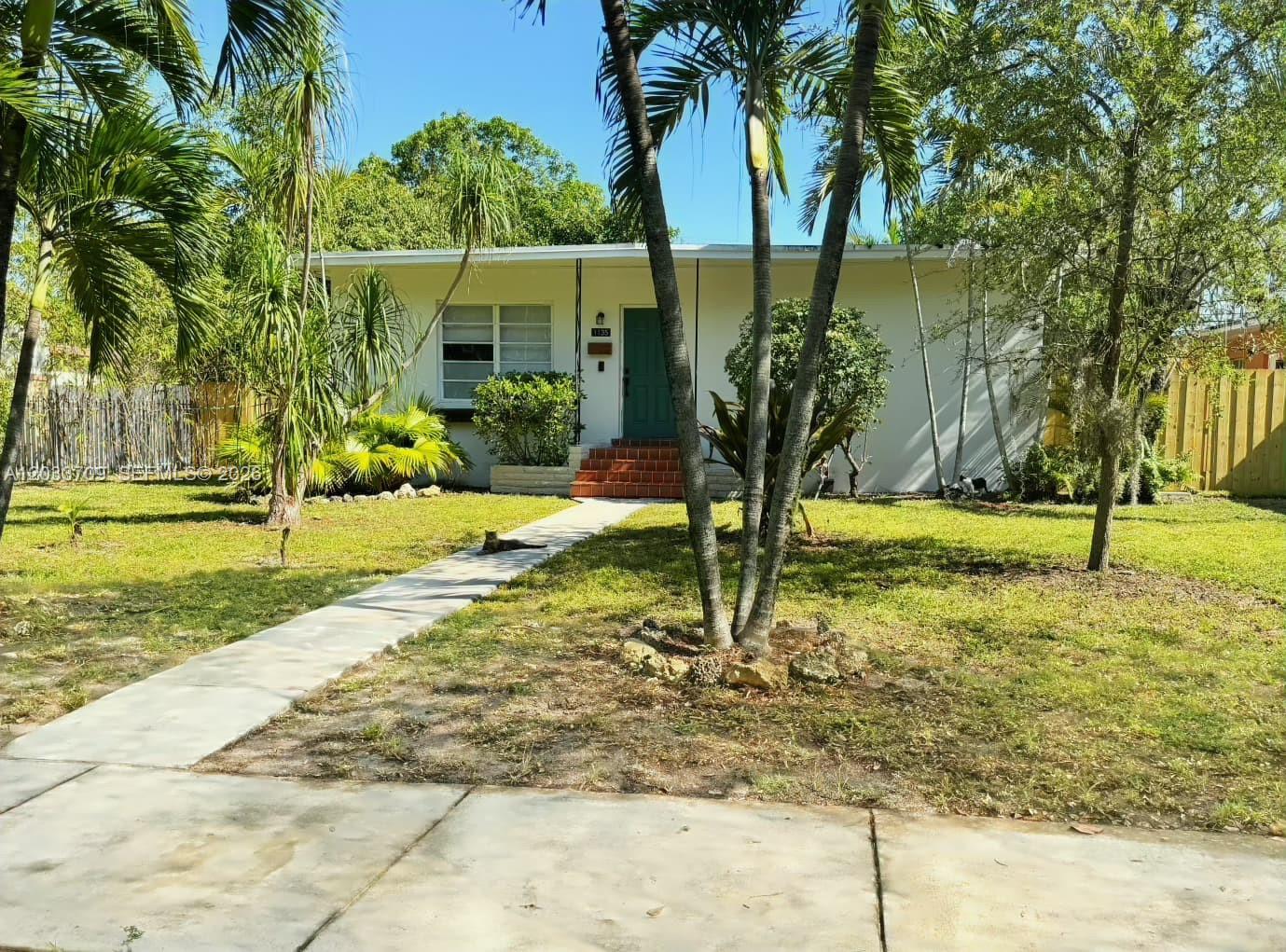 A single-story white house with a green door and palm trees in the front yard — 1135 NE 133 rd St, North Miami FL 33161, NORTH MIAMI, FL