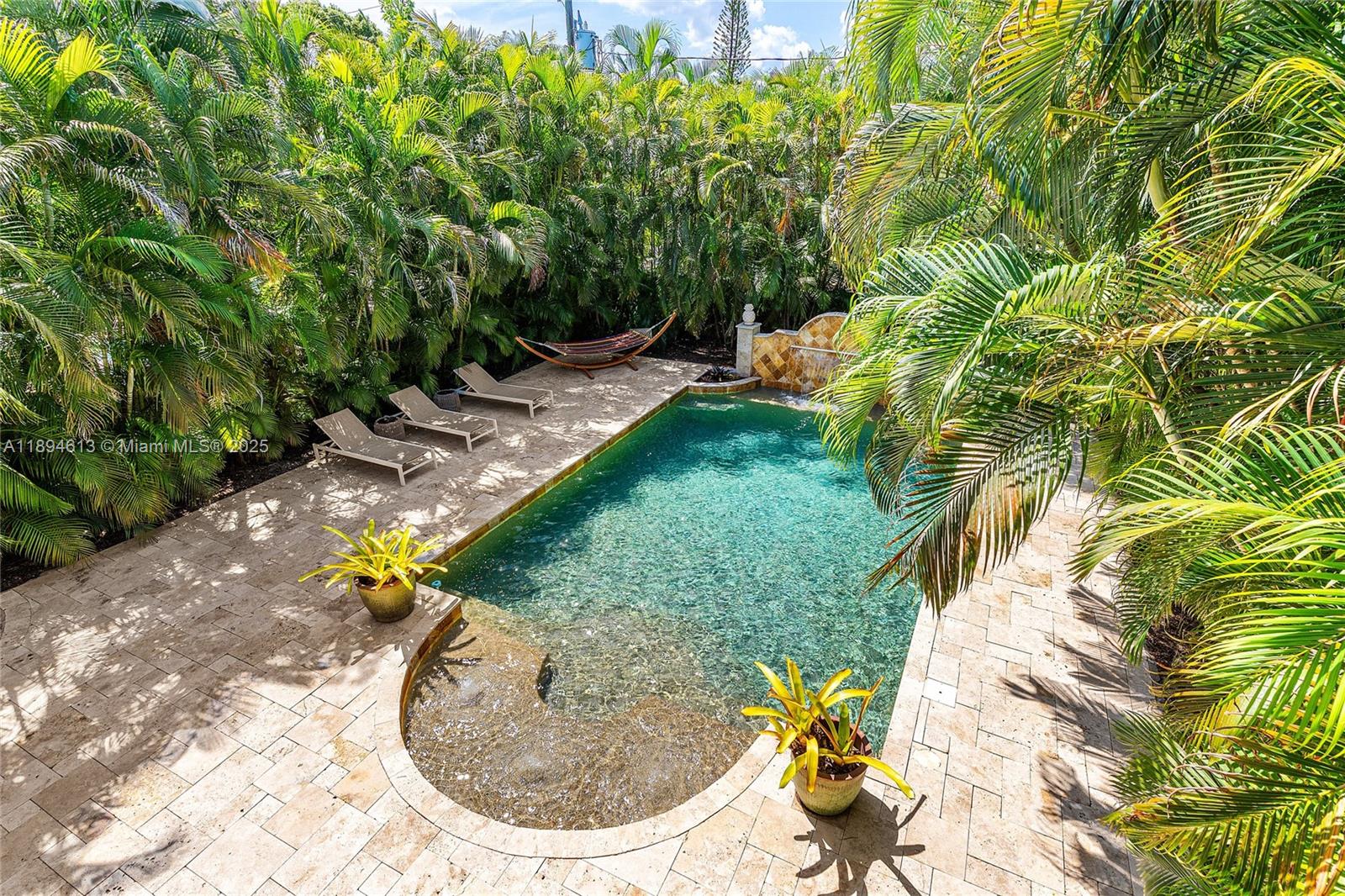 A rectangular swimming pool with a stone patio, lounge chairs, and lush tropical landscaping — 12 NE 26th St, Wilton Manors FL 33305, WILTON MANORS, FL