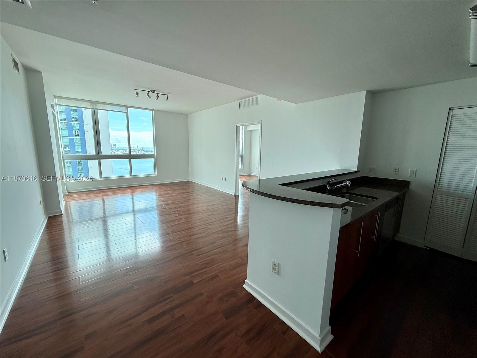 An open-concept living area features hardwood floors, a kitchen island, and floor-to-ceiling windows with water views — 300 S Biscayne Blvd # 3014, Miami FL 33131, MIAMI, FL