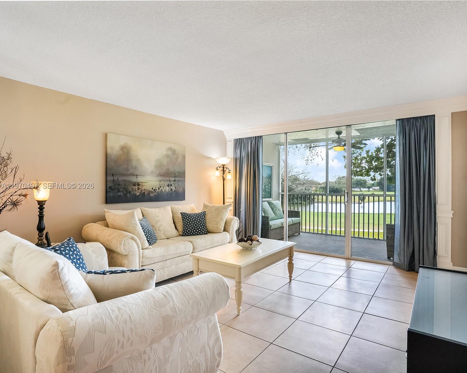 A living room with tile floors, beige walls, and a sliding door to a balcony — 2681 S Course Dr # 209, Pompano Beach FL 33069, POMPANO BEACH, FL