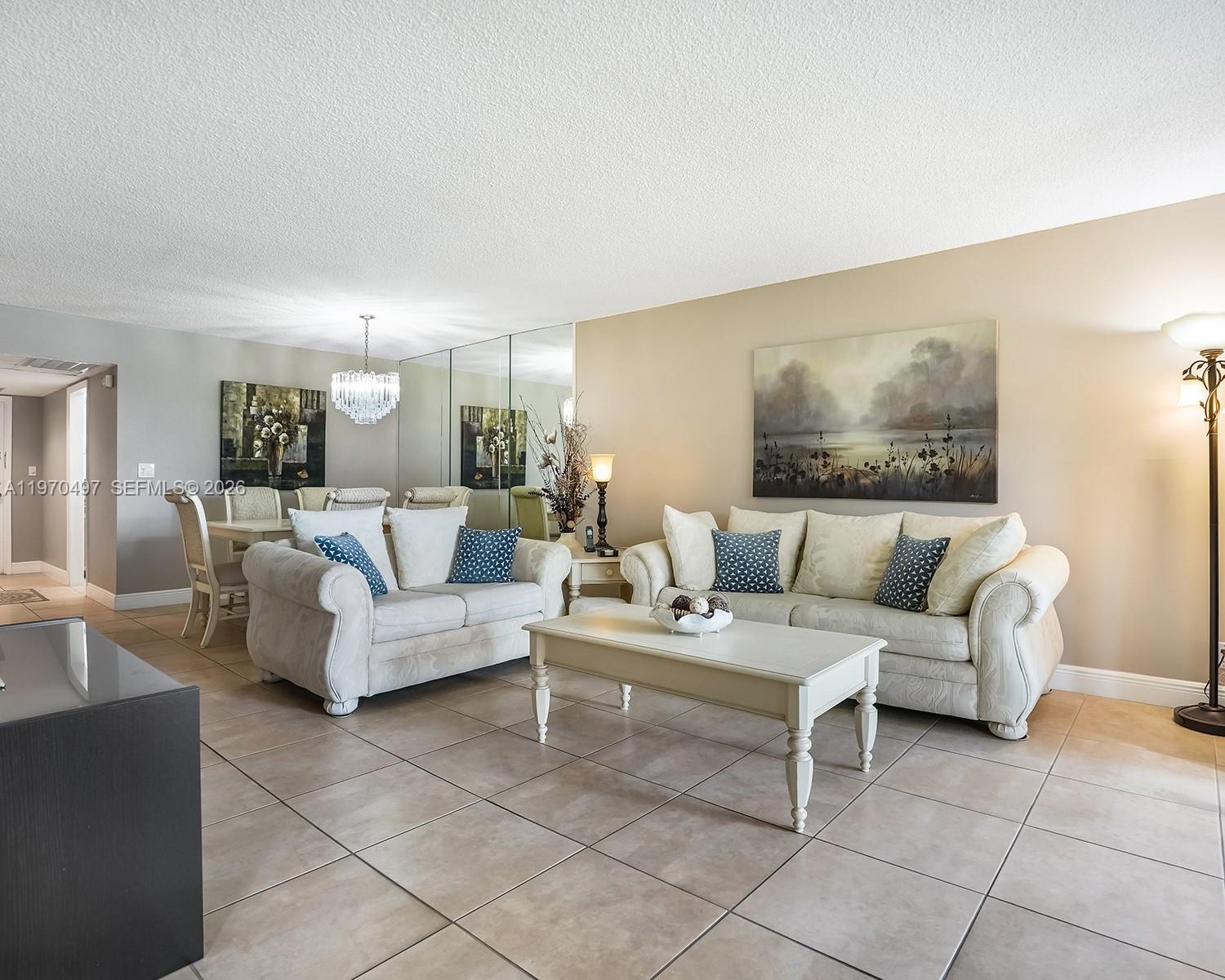 A living room features beige tile floors, two off-white sofas, a coffee table, and mirrored walls — 2681 S Course Dr # 209, Pompano Beach FL 33069, POMPANO BEACH, FL
