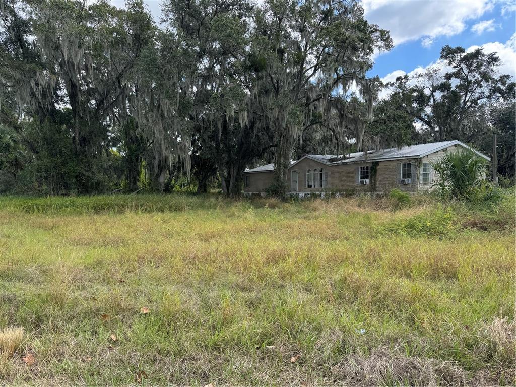A weathered mobile home sits on a grassy lot surrounded by large, moss-covered oak trees — 3721 PORTER ROAD, LITHIA, FL