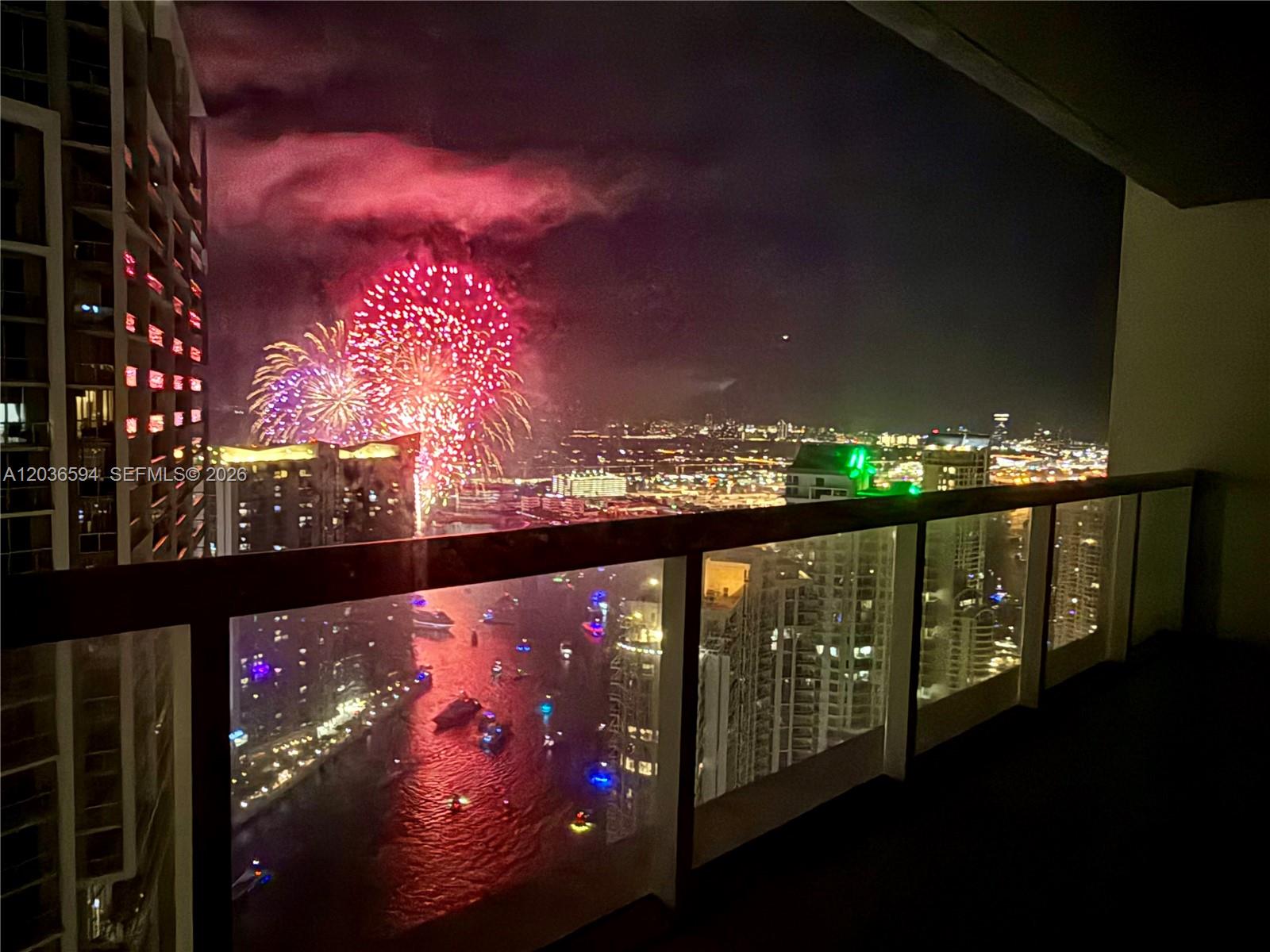 A balcony view at night shows fireworks over a city skyline and a waterway — 495 Brickell Ave # 5106, Miami FL 33131, MIAMI, FL