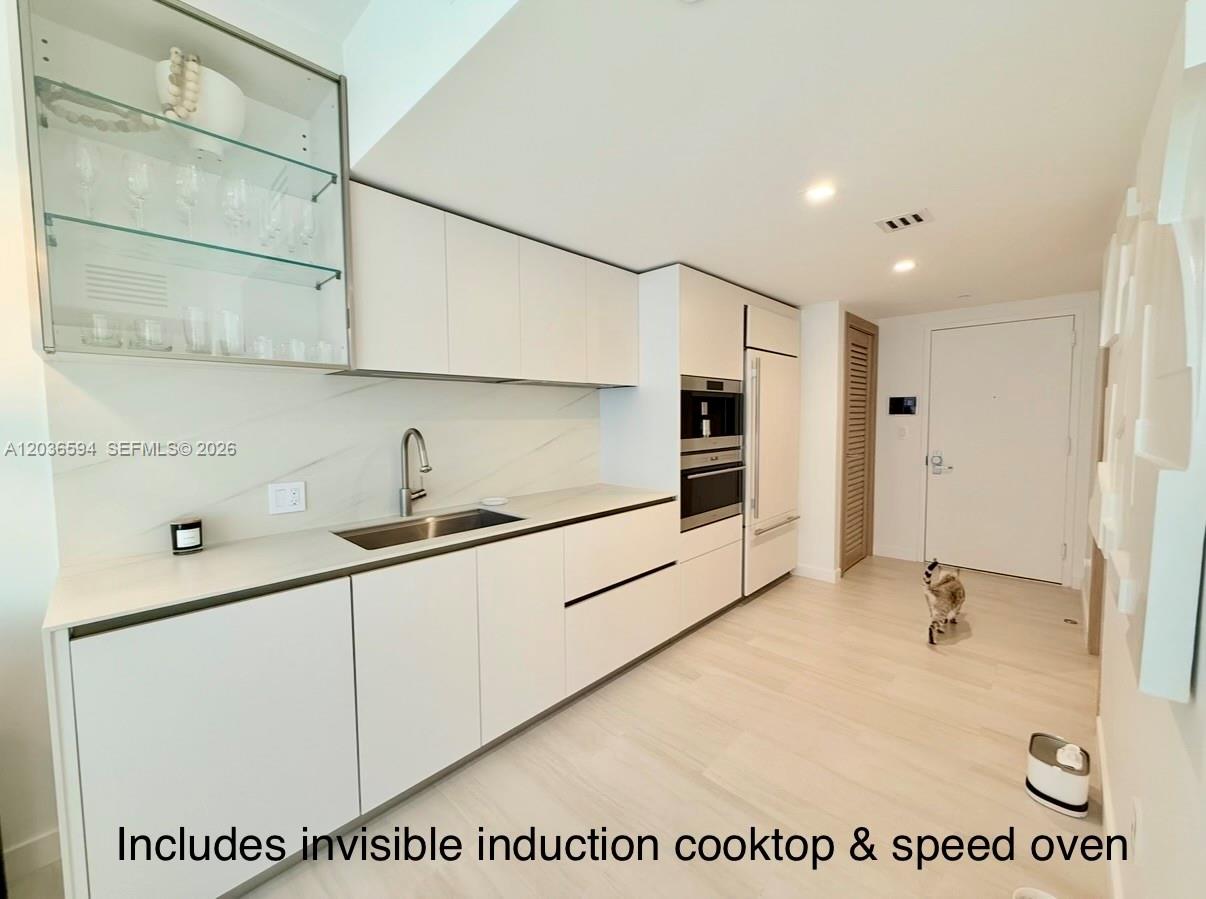 A modern white kitchen features sleek cabinetry, a glass-front display cabinet, and integrated appliances — 495 Brickell Ave # 5106, Miami FL 33131, MIAMI, FL
