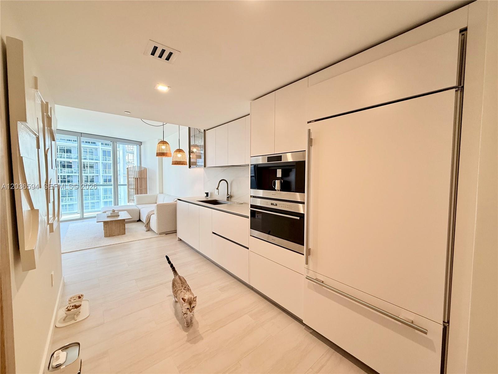 A modern kitchen with white cabinetry and integrated appliances opens into a bright living area — 495 Brickell Ave # 5106, Miami FL 33131, MIAMI, FL