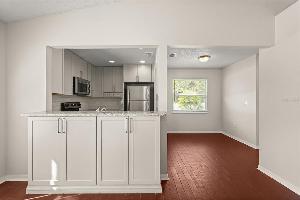 A kitchen with white cabinets and granite countertops overlooks a dining area with wood flooring — 525 PARTRIDGE DRIVE, KISSIMMEE, FL
