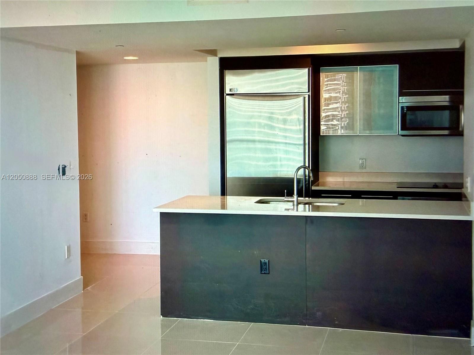 A modern kitchen features a dark island with a sink, stainless steel appliances, and cabinetry — 500 Brickell Ave # 2003, Miami FL 33131, MIAMI, FL