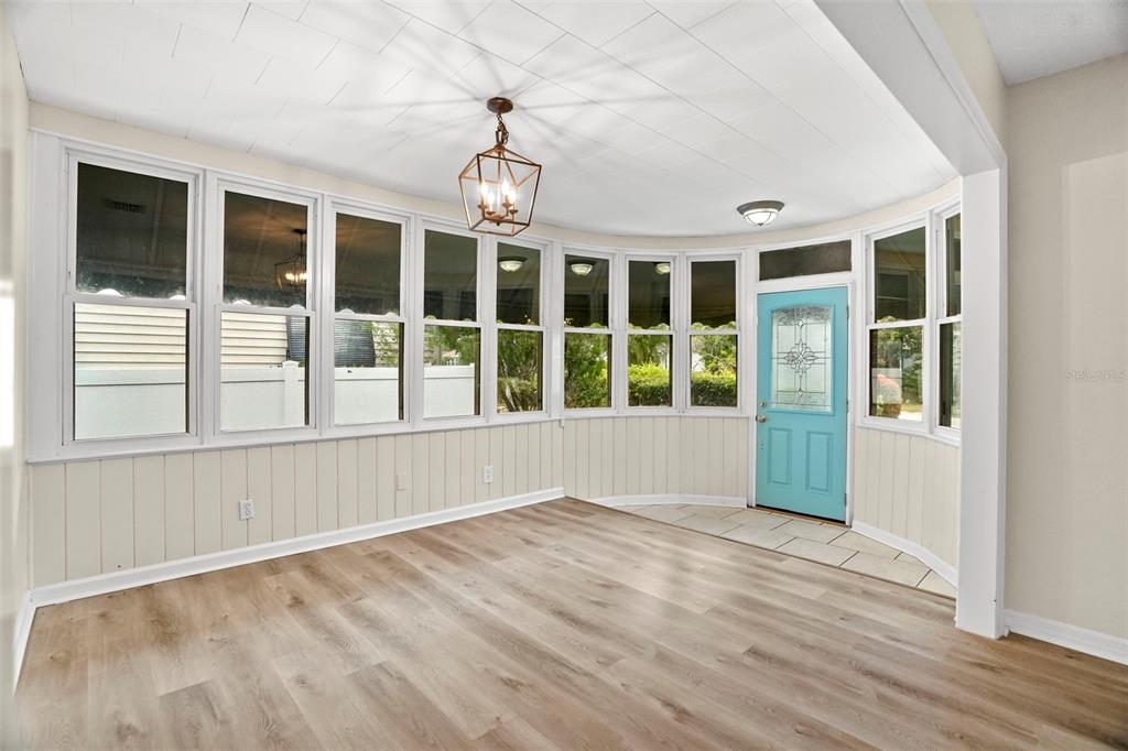 A sunroom with light wood-look flooring, white paneled walls, a geometric pendant light, and windows — 446 37TH AVENUE NE, ST PETERSBURG, FL