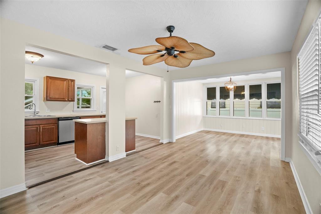 An open-concept living area with wood-look flooring, a palm-leaf ceiling fan, and an adjacent kitchen — 446 37TH AVENUE NE, ST PETERSBURG, FL