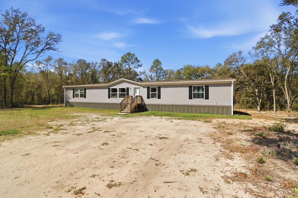 A single-story manufactured home with light gray siding sits on a large, sandy lot — 7290 NE 110TH AVENUE, BRONSON, FL