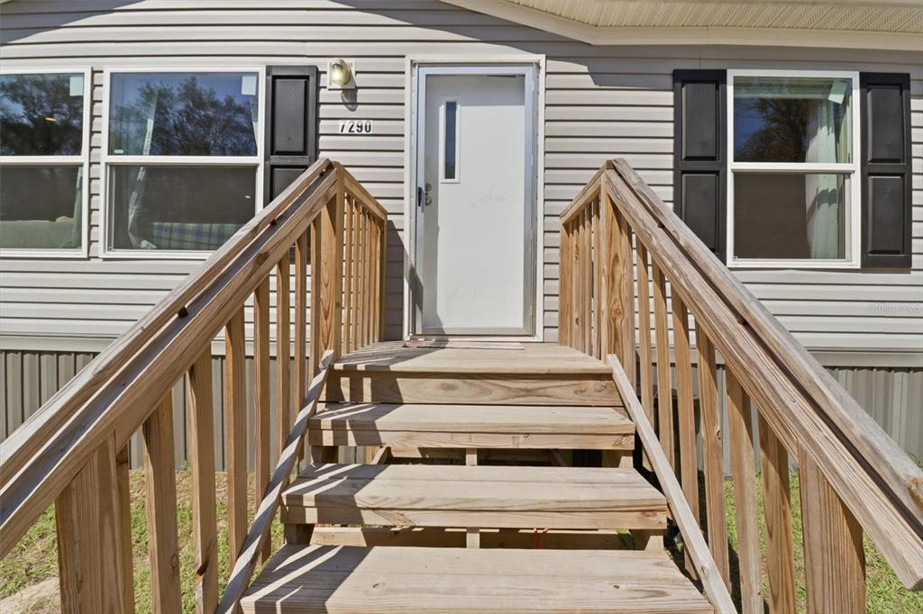 A wooden staircase leads to the front door of a house with gray siding — 7290 NE 110TH AVENUE, BRONSON, FL