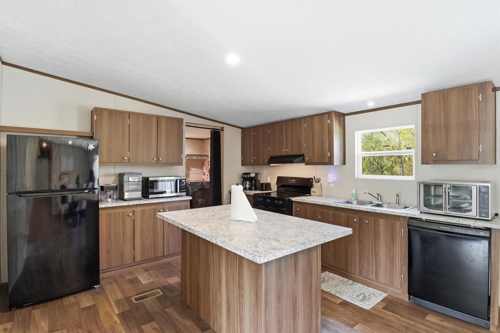 A kitchen features wood-tone cabinets, a central island with a stone countertop, and black appliances — 7290 NE 110TH AVENUE, BRONSON, FL