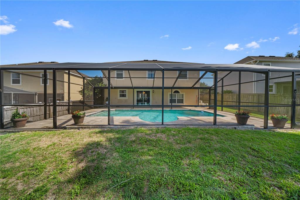 A backyard features a swimming pool enclosed by a screened lanai behind a two-story house — 14308 NW 161ST AVENUE, ALACHUA, FL
