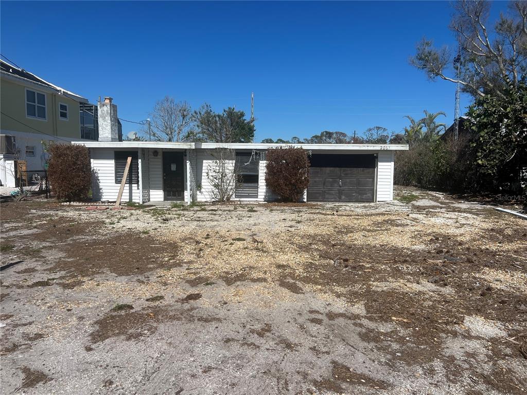 A single-story white house with a garage and a dirt yard under a clear sky — 2061 S PINE ST, ENGLEWOOD, FL