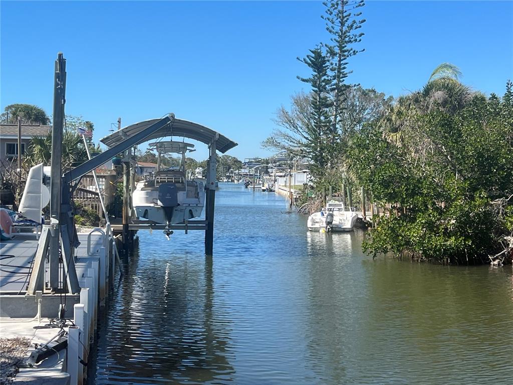 A boat on a lift sits in a canal lined with trees and other boats — 2061 S PINE ST, ENGLEWOOD, FL