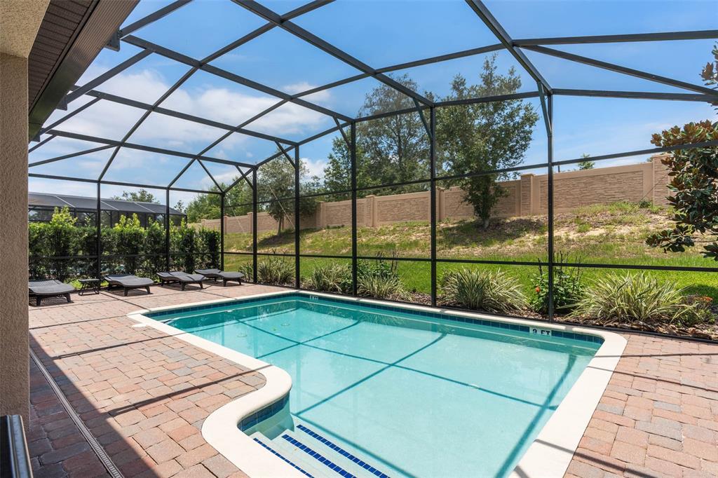A rectangular swimming pool sits inside a screened-in patio with brick pavers and lounge chairs — 1476 MOON VALLEY DRIVE, DAVENPORT, FL