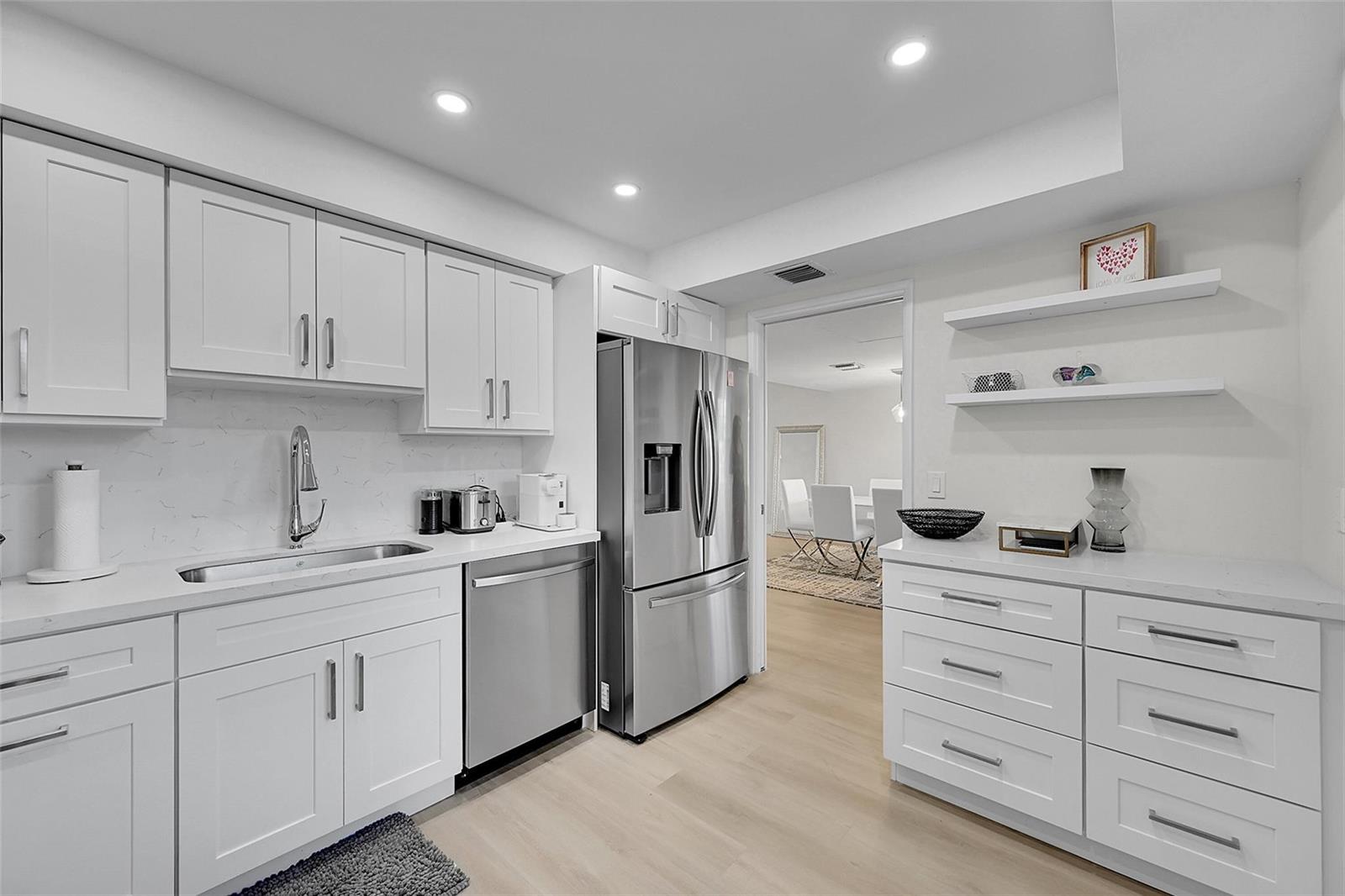 A modern kitchen features white cabinetry, stainless steel appliances, and light wood flooring — 555 Oaks Lane # 311, Pompano Beach FL 33069, POMPANO BEACH, FL