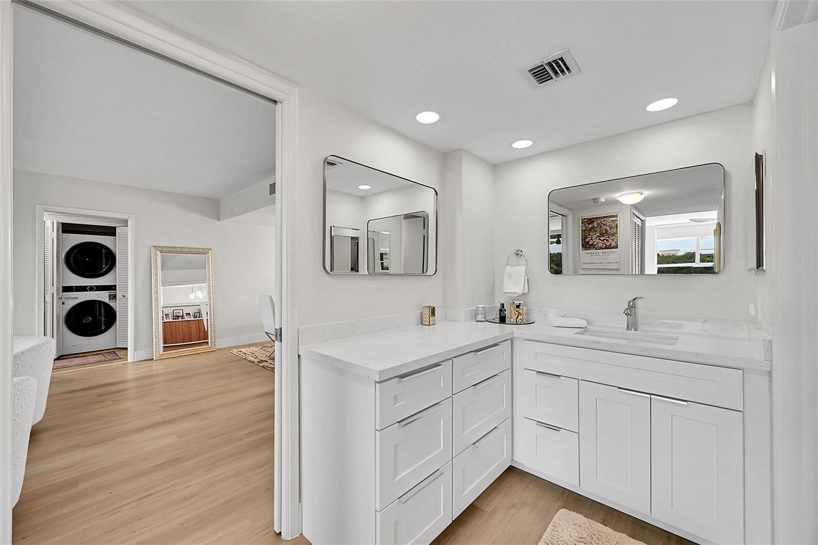 A white bathroom vanity with a sink and mirrors sits beside a doorway to a room — 555 Oaks Lane # 311, Pompano Beach FL 33069, POMPANO BEACH, FL