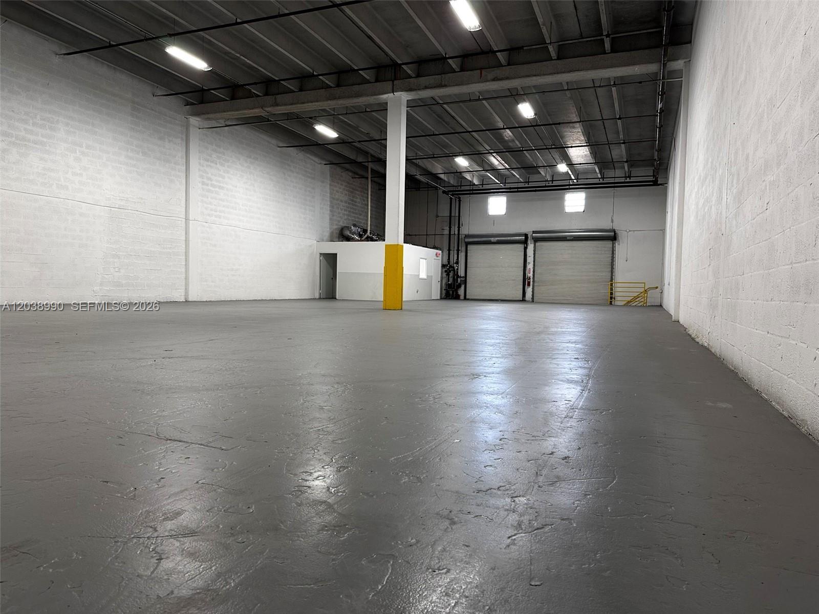 An empty industrial warehouse features gray concrete floors, white block walls, and two roll-up doors — MEDLEY, FL