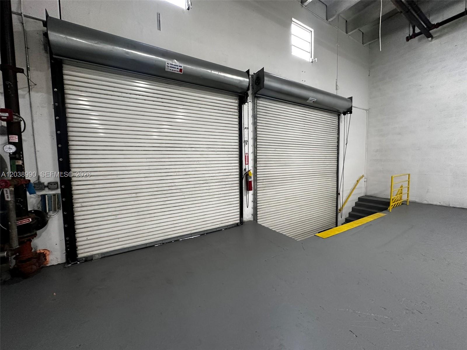 An industrial space features two large roll-up metal doors, a concrete floor, and stairs — MEDLEY, FL