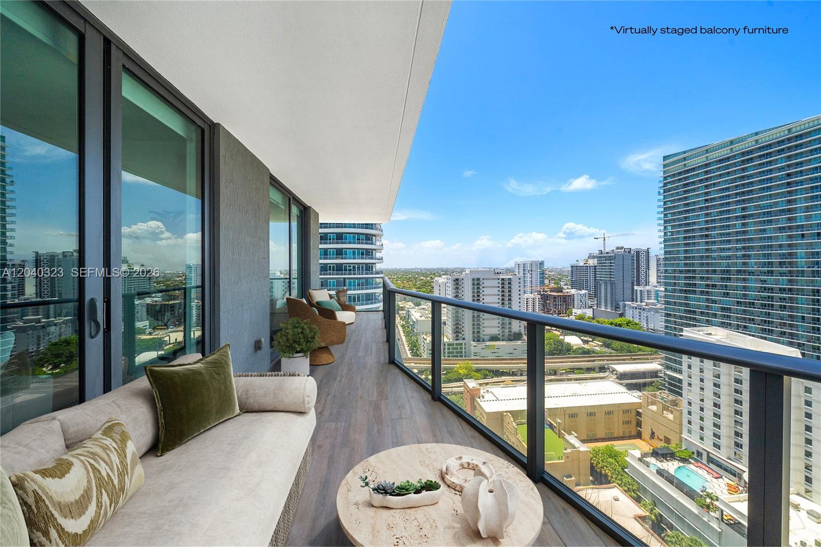 A high-rise balcony features wood-look flooring, glass railings, and a view of city buildings — 1300 S Miami Ave # 2110, Miami FL 33130, MIAMI, FL