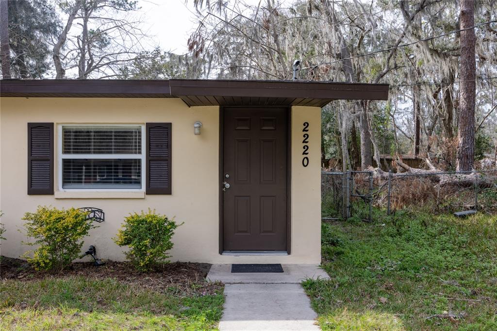 The exterior of a house features a brown door, a window with shutters, and landscaping — 2220 SE 46TH TERRACE, GAINESVILLE, FL
