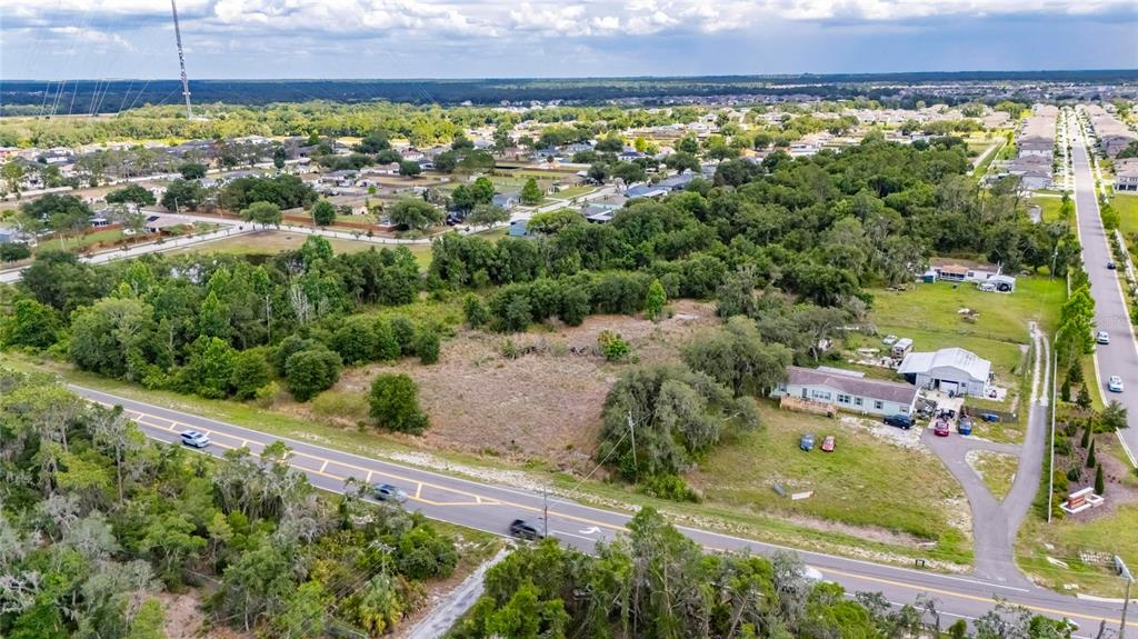 An aerial view shows a vacant lot with a house and garage beside a road — 13311 RHODINE ROAD, RIVERVIEW, FL
