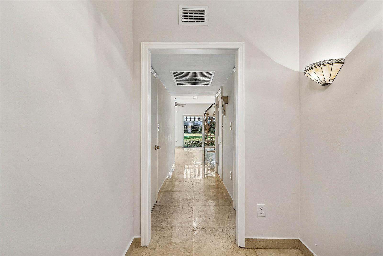 A hallway with beige tile flooring leads toward a doorway revealing a spiral staircase — 2000 S Ocean Boulevard # Y1, Delray Beach FL 33483, DELRAY BEACH, FL