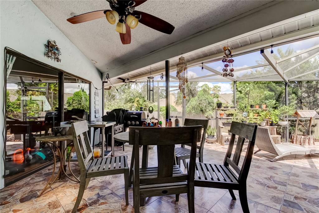 A screened-in patio features a dining set, ceiling fan, and tiled flooring overlooking a backyard — 1800 SAGEBRUSH ROAD, PLANT CITY, FL