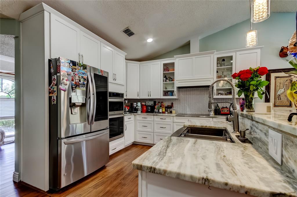 A kitchen features white cabinets, stainless steel appliances, marble countertops, and wood-look flooring — 1800 SAGEBRUSH ROAD, PLANT CITY, FL