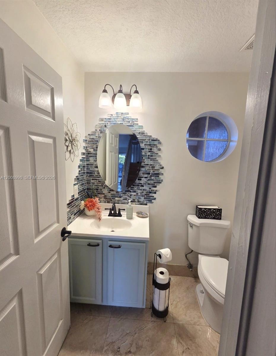 A small bathroom features a vanity with a blue cabinet, mosaic tile backsplash, and toilet — 16504 SW 71st Ter, Miami FL 33193, MIAMI, FL