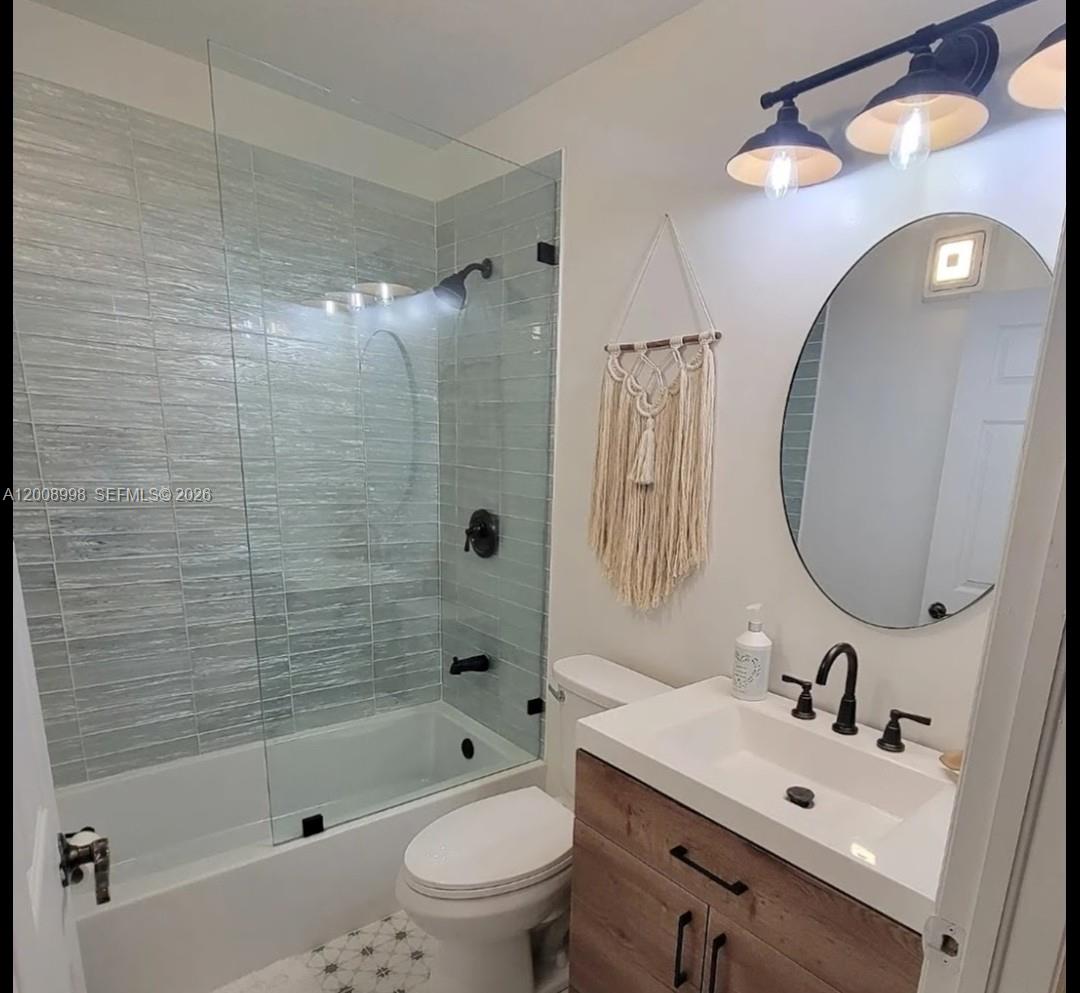 A bathroom features a wood vanity, oval mirror, glass-enclosed tub, and textured blue wall tiles — 16504 SW 71st Ter, Miami FL 33193, MIAMI, FL