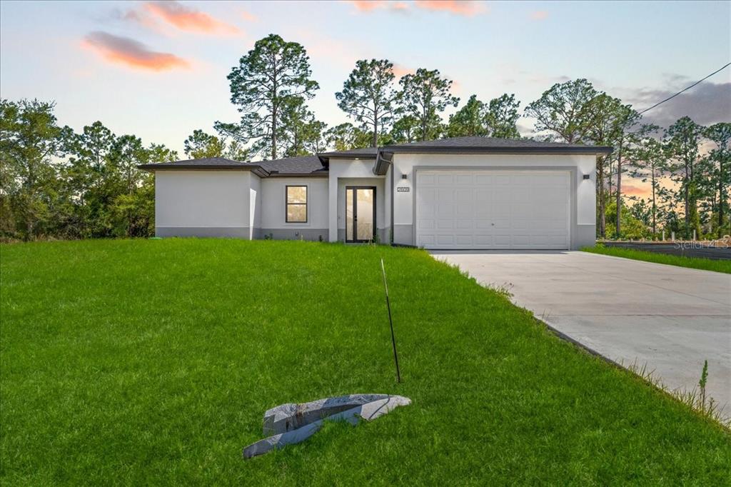 A single-story house with a white stucco exterior, a two-car garage, and a front lawn — 2914 67TH STREET W, LEHIGH ACRES, FL