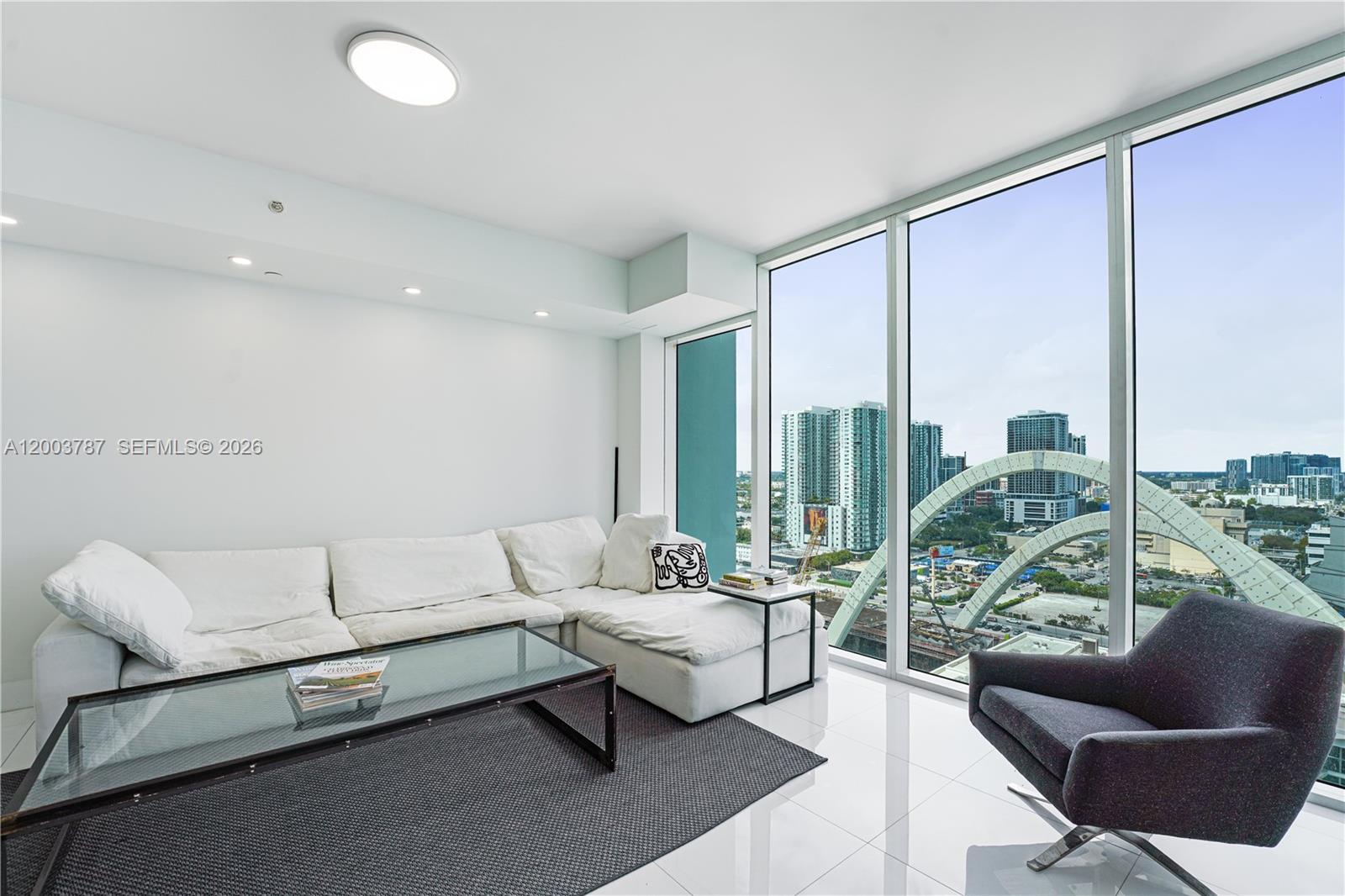 A modern living room features a white sectional sofa, glass coffee table, and floor-to-ceiling windows — 1040 Biscayne Blvd # 1905, Miami FL 33132, MIAMI, FL