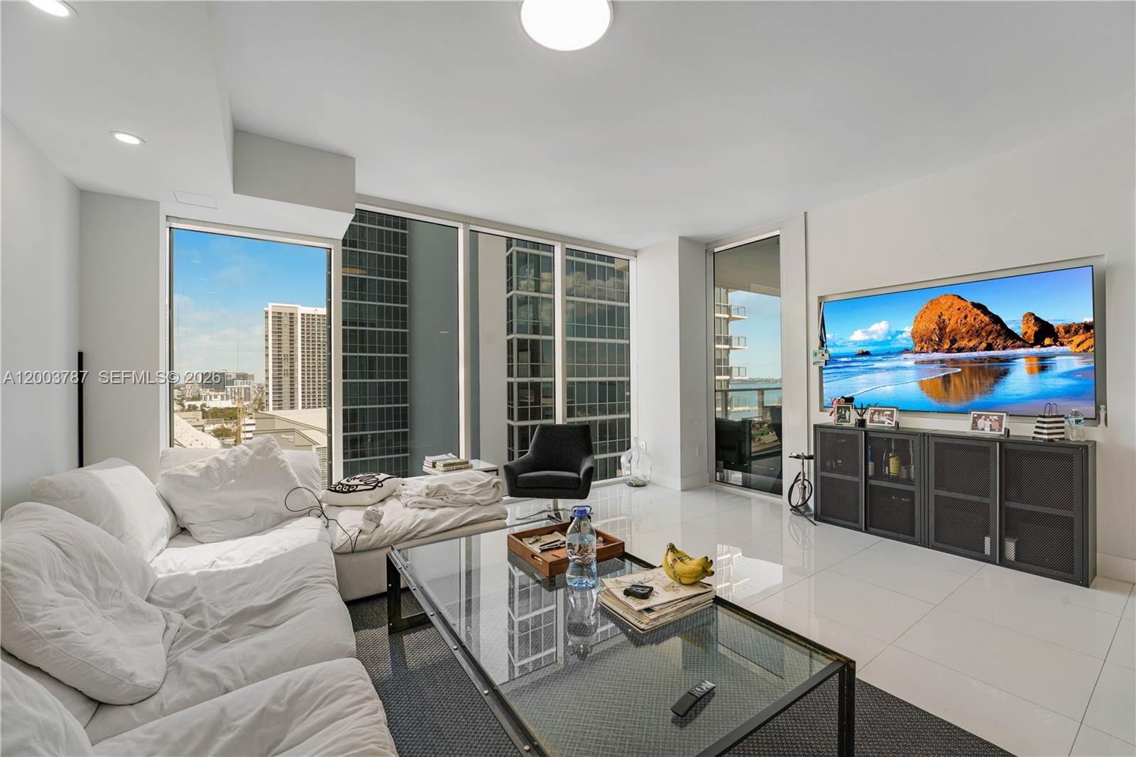 A modern living room features a white sofa, glass coffee table, and floor-to-ceiling windows — 1040 Biscayne Blvd # 1905, Miami FL 33132, MIAMI, FL