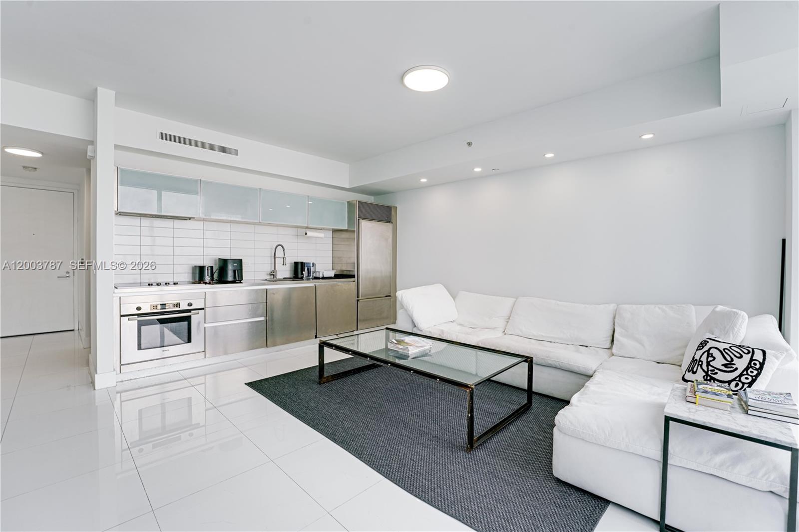 A modern studio apartment features a white kitchen, stainless steel appliances, and a white sofa — 1040 Biscayne Blvd # 1905, Miami FL 33132, MIAMI, FL