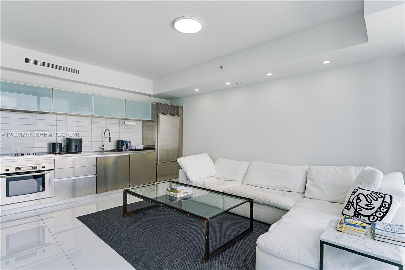 A modern studio apartment features a stainless steel kitchen and a white sectional sofa — 1040 Biscayne Blvd # 1905, Miami FL 33132, MIAMI, FL