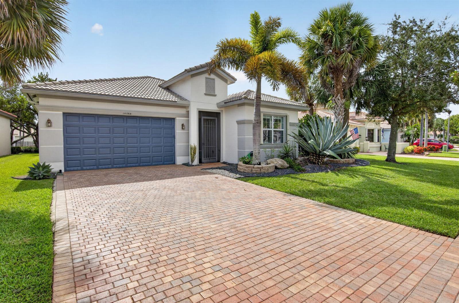 A single-story house with a blue garage door, brick paver driveway, and palm trees — 14788 Strand Lane, Delray Beach FL 33446, DELRAY BEACH, FL