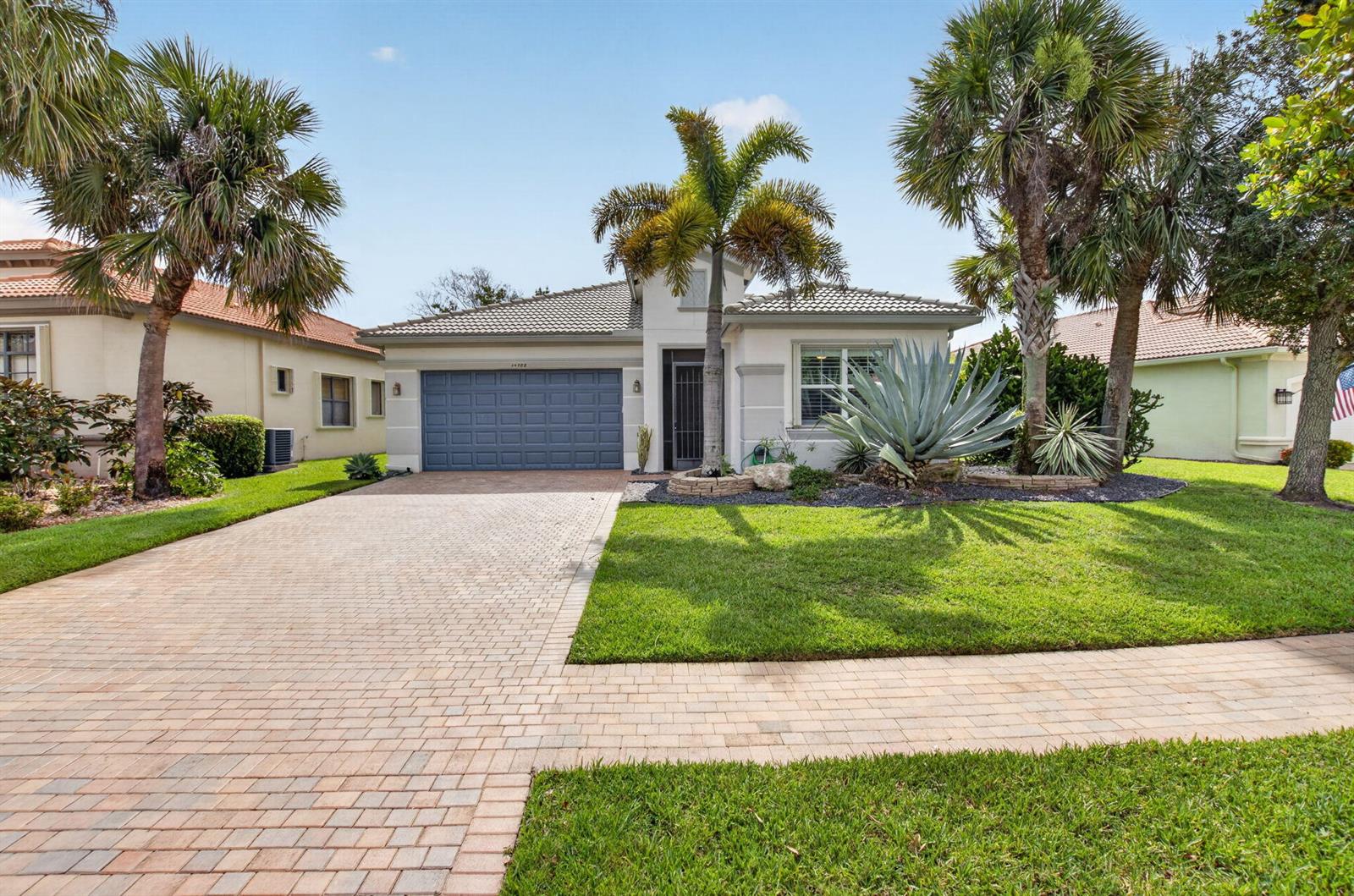 A single-story house with a blue garage door, paver driveway, and palm trees in front — 14788 Strand Lane, Delray Beach FL 33446, DELRAY BEACH, FL