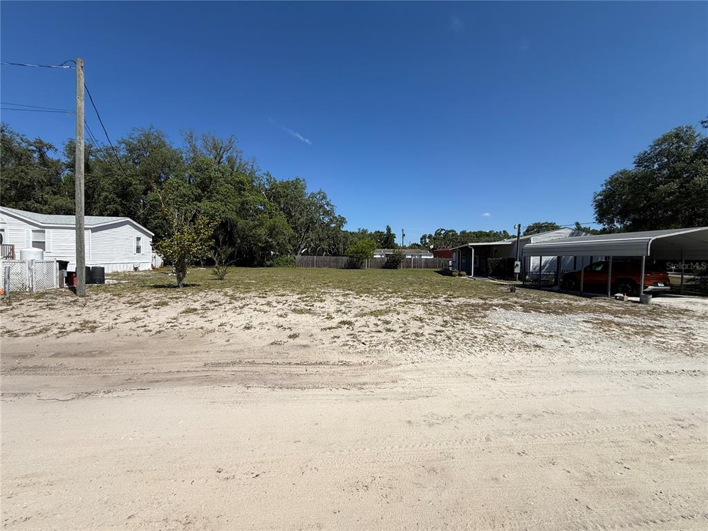 A vacant, sandy lot sits between two residential properties under a clear blue sky — CODEL LOOP, NEW PORT RICHEY, FL