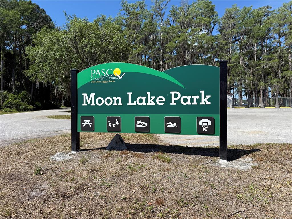 A sign for Moon Lake Park stands in a grassy area with trees in the background — CODEL LOOP, NEW PORT RICHEY, FL