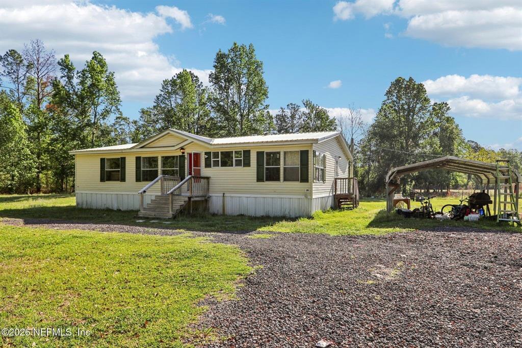 A single-story manufactured home with light siding sits on a gravel lot near trees — 14070 JOHN WILLIAMS ROAD, SANDERSON, FL