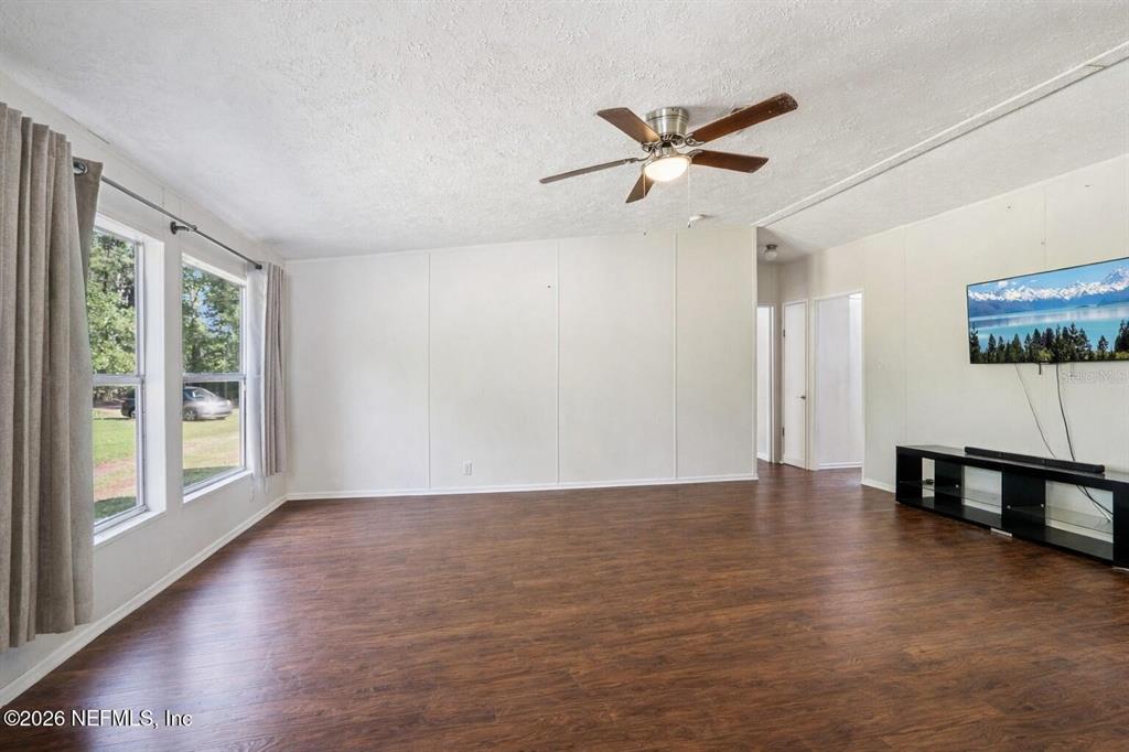 A living room features wood-look flooring, white walls, a ceiling fan, and a wall-mounted television — 14070 JOHN WILLIAMS ROAD, SANDERSON, FL