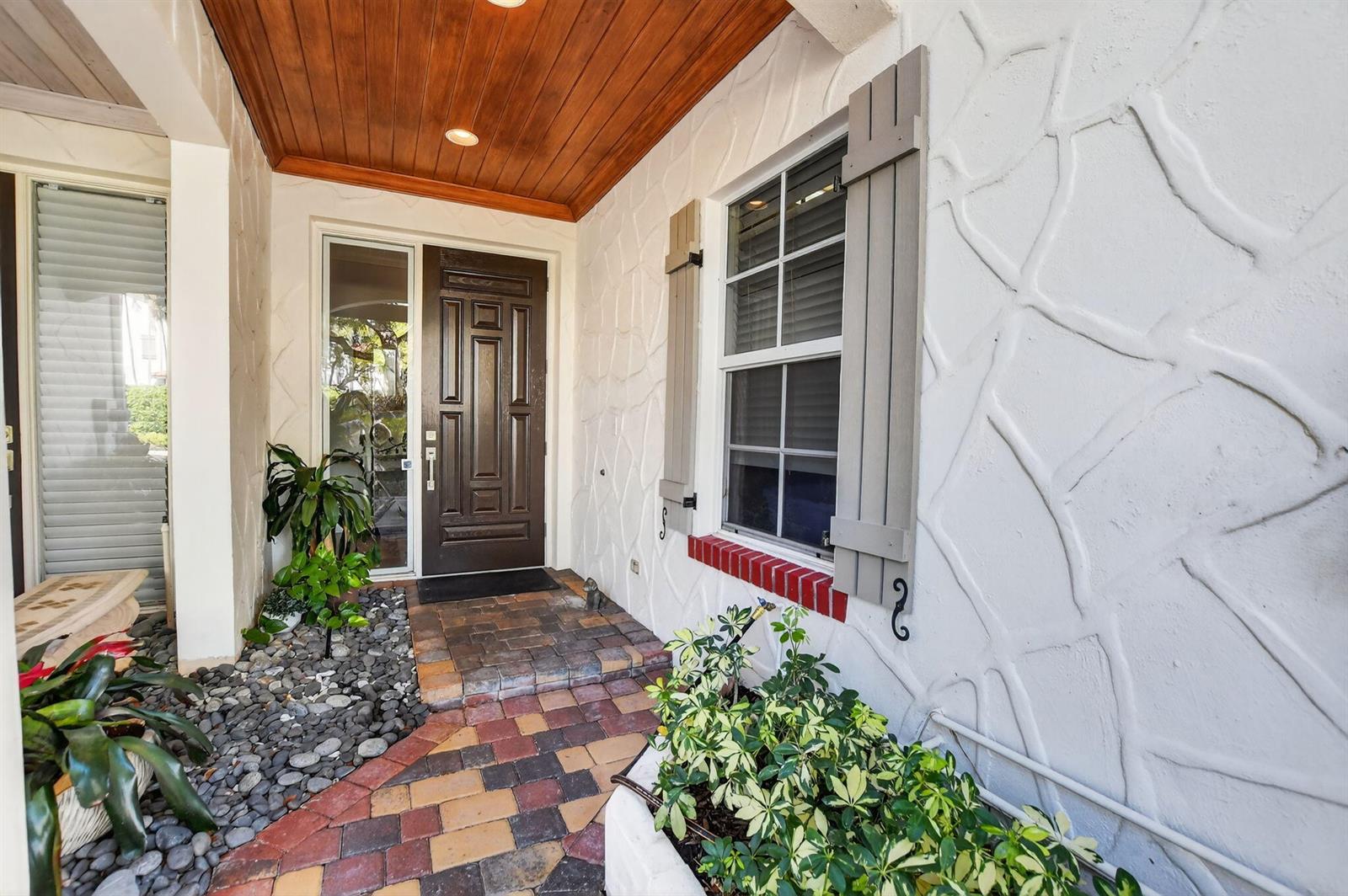 A front entryway features a dark wood door, stone-textured walls, and a brick-paved porch — 1535 Estuary Trail, Delray Beach FL 33483, DELRAY BEACH, FL