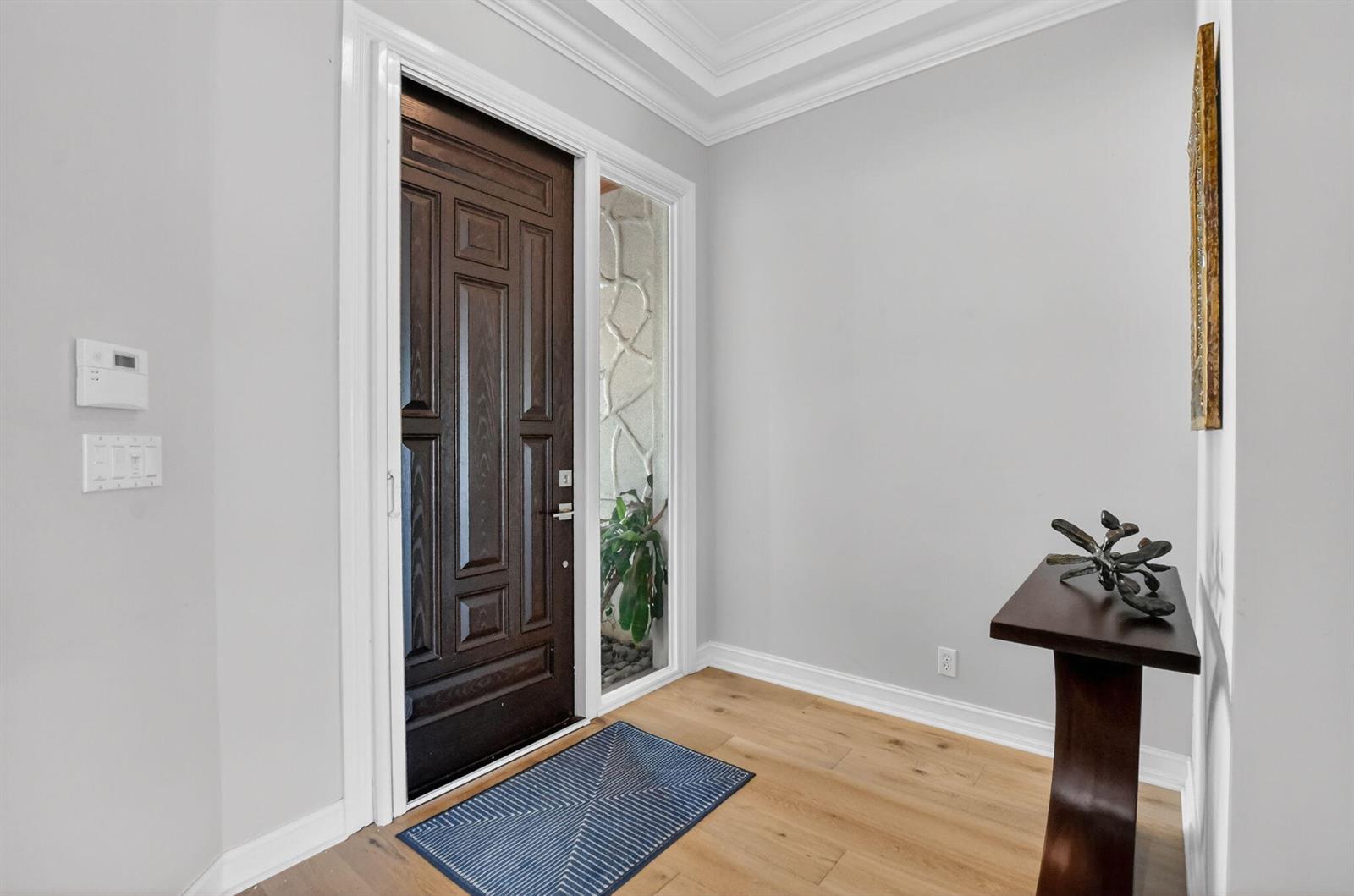 An entryway features a dark wood door, light hardwood floors, and a small console table — 1535 Estuary Trail, Delray Beach FL 33483, DELRAY BEACH, FL